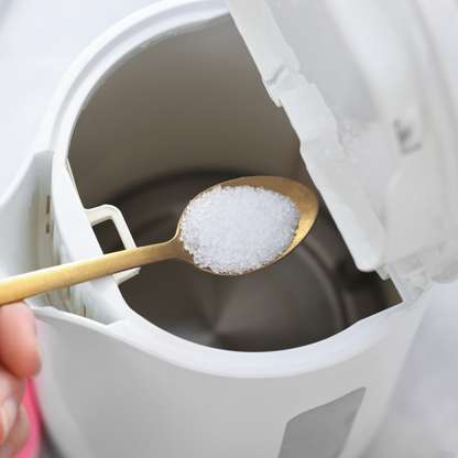 A kettle with a spoon full of Citric Acid being poured in as a natural descaler