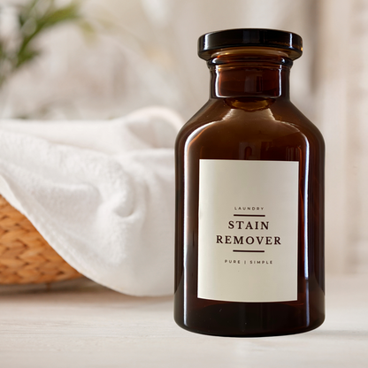 A vintage look amber glass apothecary jar with crisp white label Stain Remover infront of basket with white towles. Jar is full of sodium percarbonate for natural cleaning