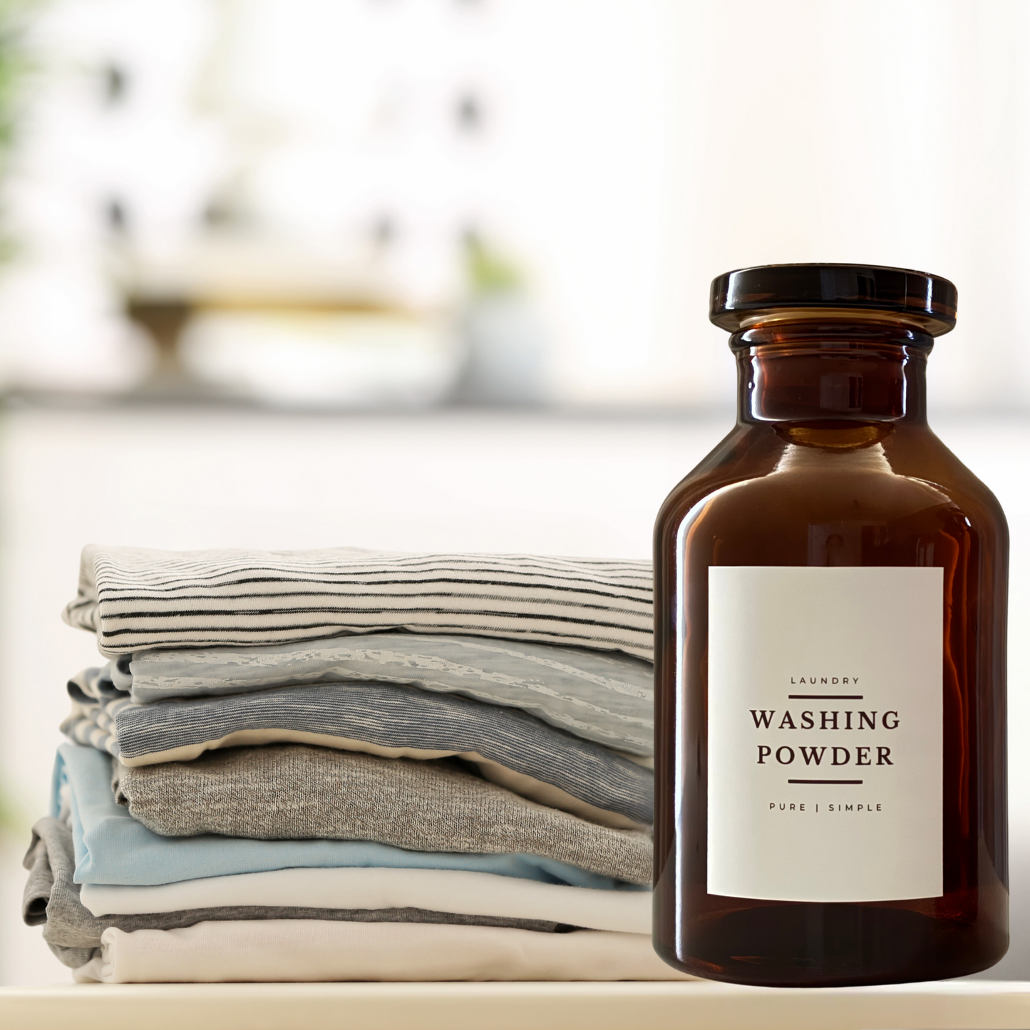 A vintage style amber glass Apothecary jar with crisp white Washing Powder Label in front of folded clean clothes. Filled with handmade Laundry Washing Powder made by Under Your Sink