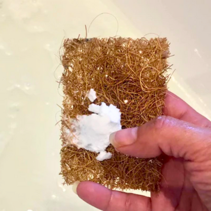 A hand holding a Safix scrub pad with the white multipurpose cleaning paste like gumption on it over a bathtub about to clean it.