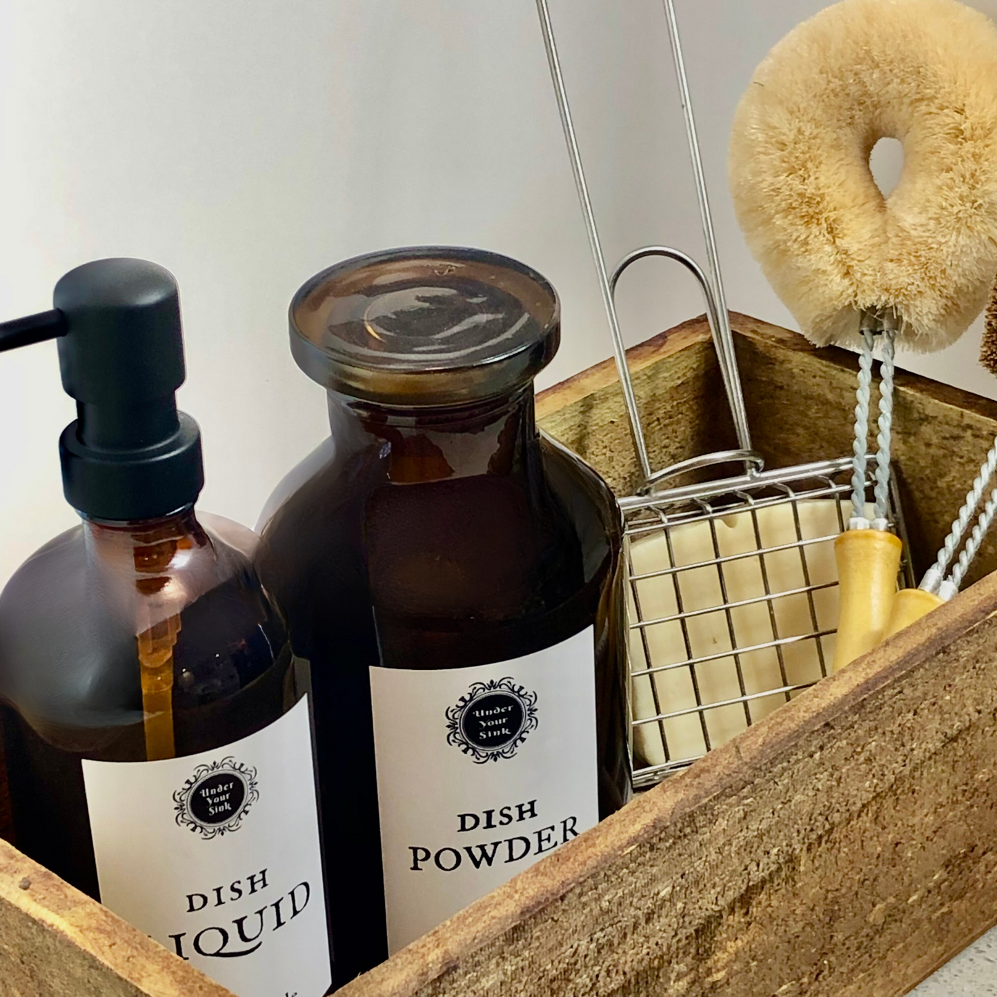 a sink caddy with amber glass pump bottle with dish Liquid label and Amber glass Apothecary Jar and metal soap swisher cage and eco friendly dish brushes